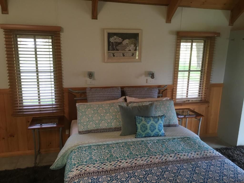 A bedroom with a bed, two nightstands, a framed picture on the wall, and wooden window blinds.