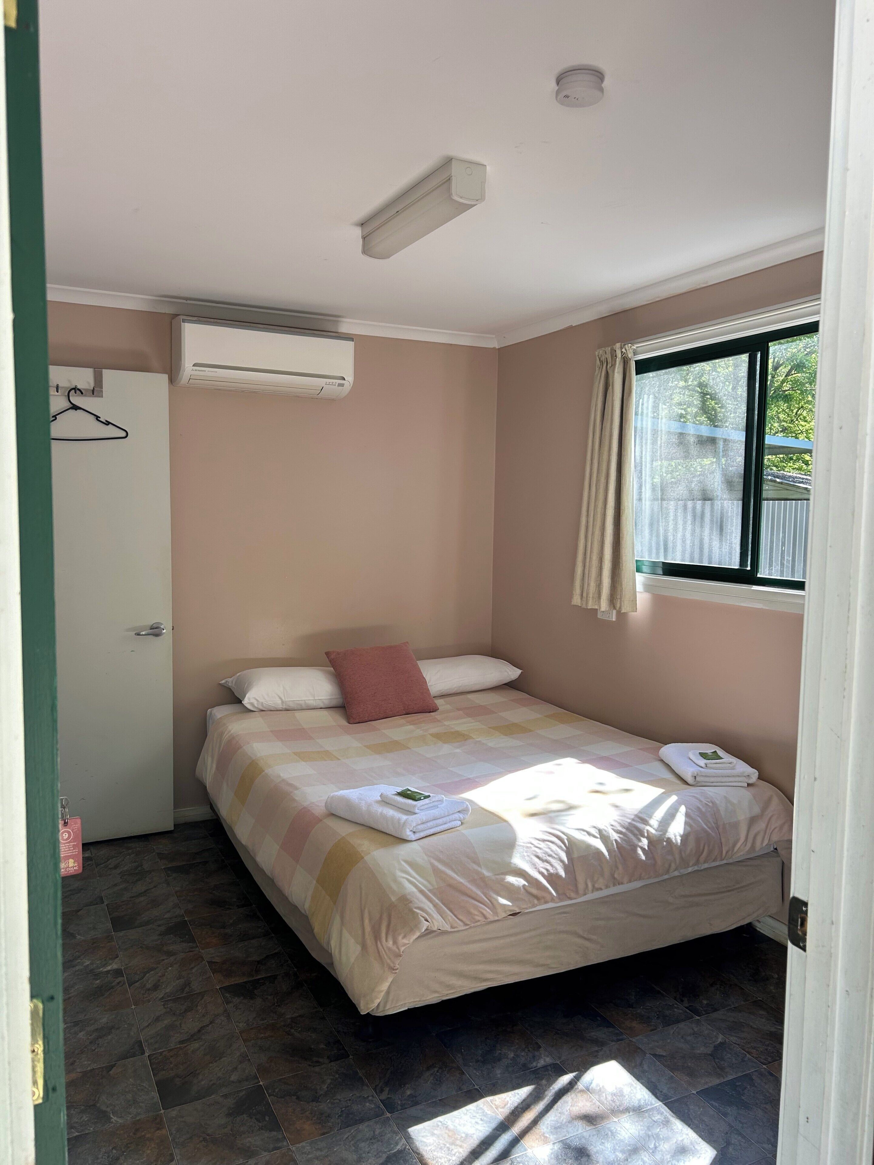 Un dormitorio con cama, ventana, puerta y aire acondicionado.