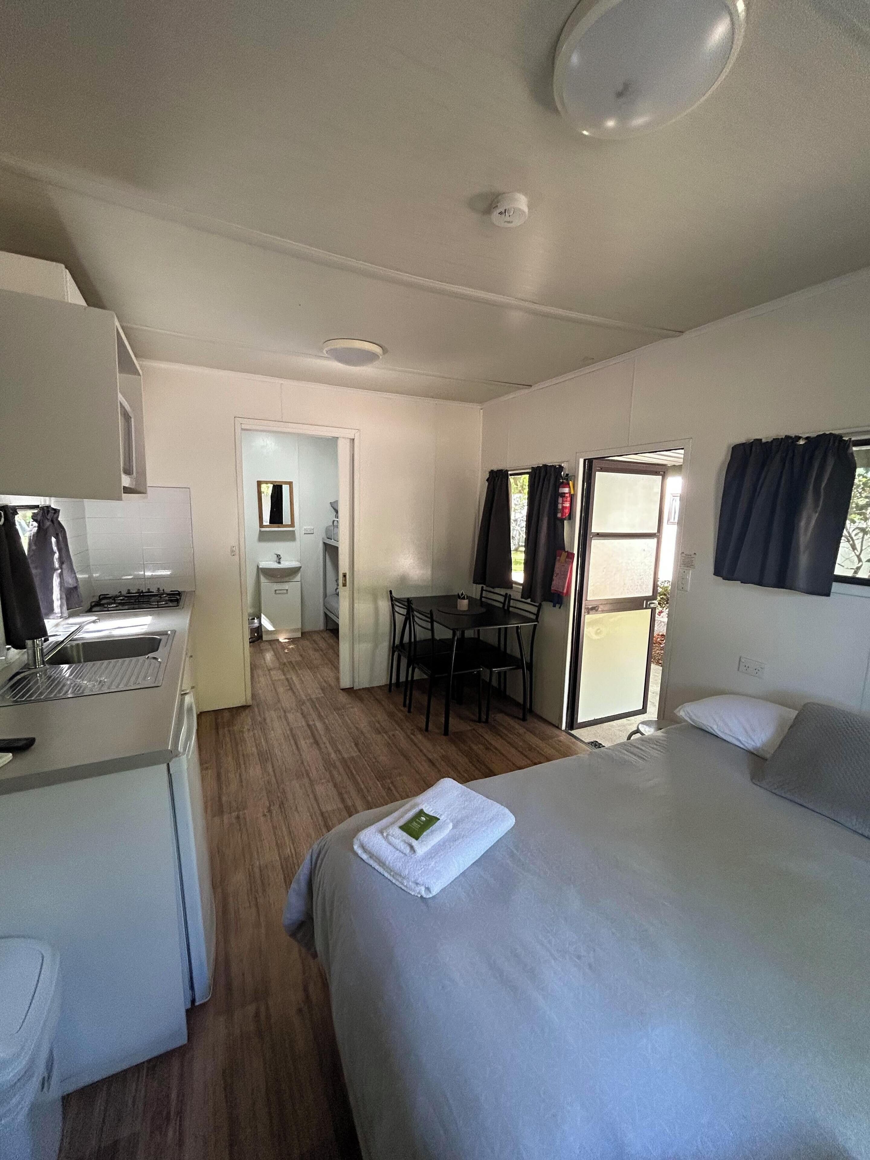 Una camera d'albergo compatta con angolo cottura, un letto, un piccolo tavolo da pranzo e un bagno separato.