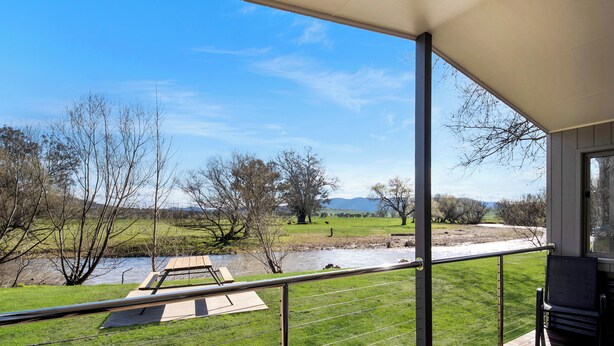 Un balcón con vista a un río, campos cubiertos de hierba y árboles.