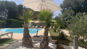 Un espace piscine aménagé avec des chaises longues, des palmiers et des parasols.