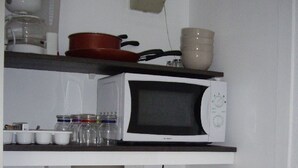 Una cocina con microondas, estufa, lavaplatos y repisas con frascos y tazas.