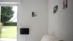 Una habitación con un sofá blanco, un televisor de pantalla plana montado en la pared y un pequeño marco con una flor.