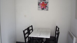 Un pequeño comedor con una mesa blanca y cuatro sillas negras. En la pared, un cuadro enmarcado con una flor rosa.