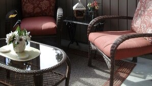 Ein Wintergarten mit Korbstühlen, einem kleinen Tisch und Blick auf Bäume.