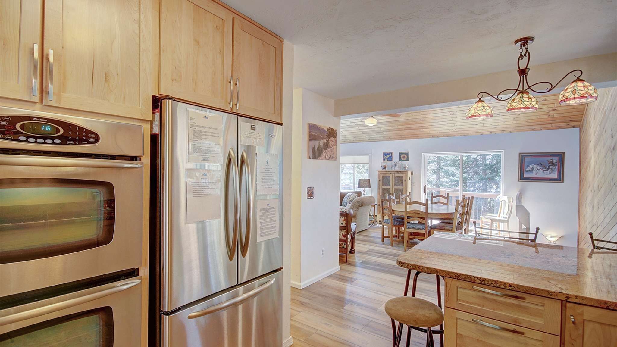 Una cocina con electrodomésticos de acero inoxidable, armarios de madera, una zona de comedor con mesa y sillas, y una araña.