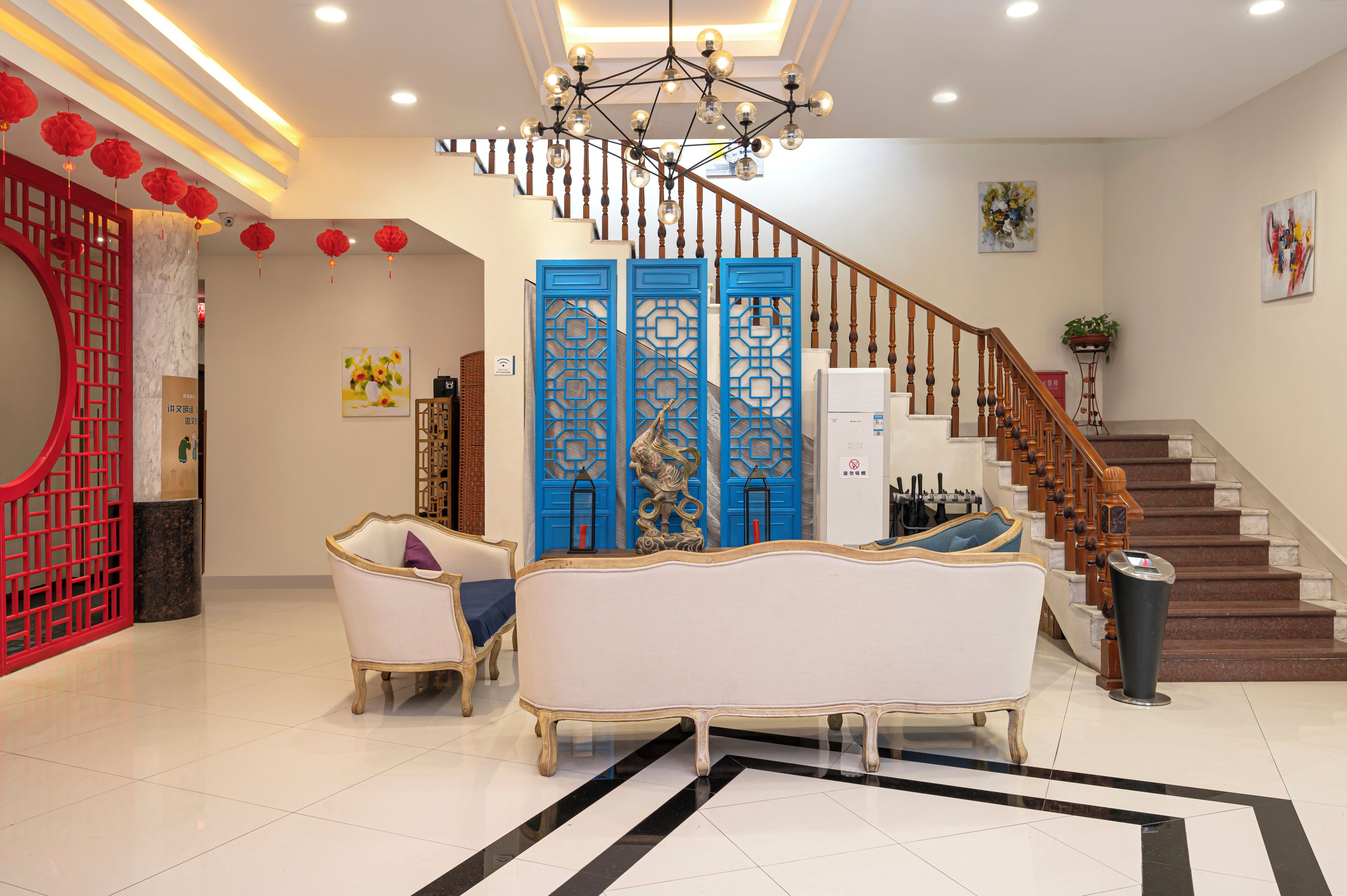 A spacious lobby with a grand staircase, elegant white sofas, and a decorative red and blue partition.