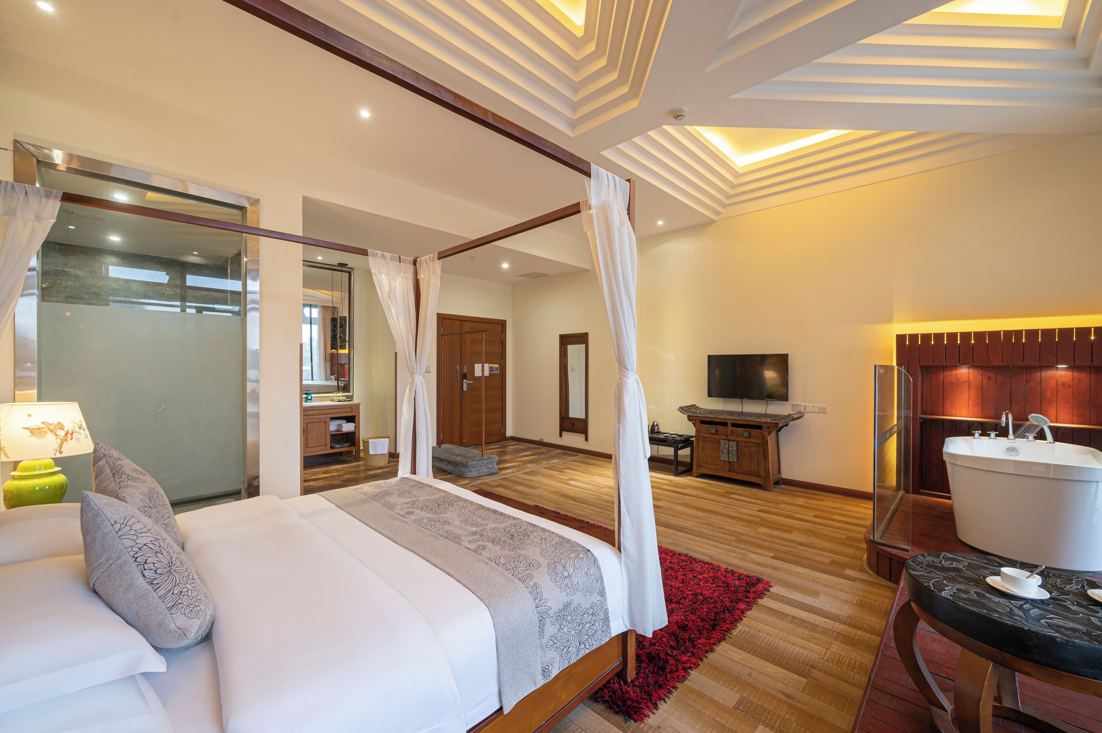 A modern hotel room with a four-poster bed, a sitting area with a bathtub, and a television.