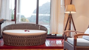 A wicker sofa with a cushion, a floor lamp, and a view of a mountainous landscape through large windows. - Guilin Crystal Crescent Moon Hotel (Guilin)