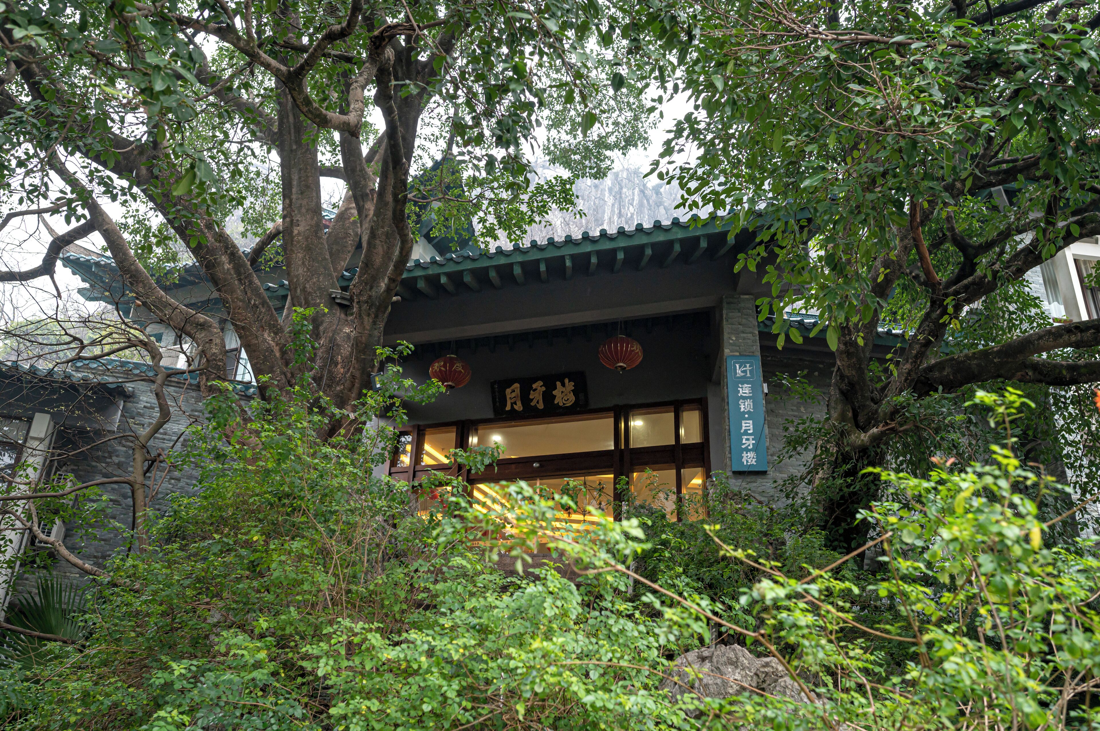 A traditional building with a dark roof and wooden structure, surrounded by dense foliage.