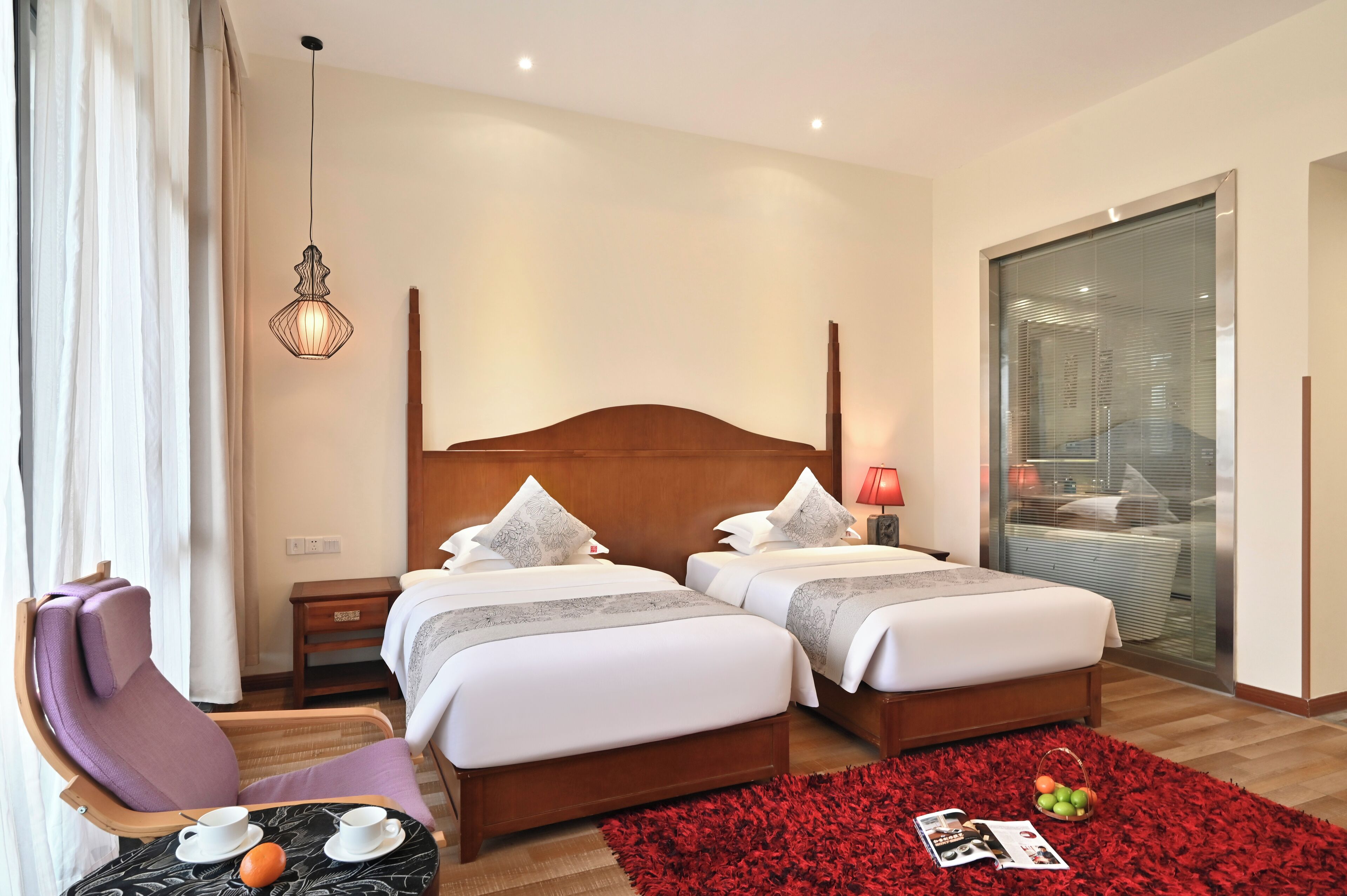 A hotel room with two beds, a wooden headboard, a red rug, a small table with a tray, and a hanging light fixture.