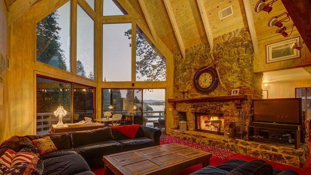 A cozy living room with a stone fireplace, leather sofas, and large windows overlooking a scenic view.