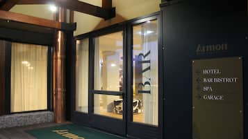 Ingresso di un hotel con un tappeto verde, segnaletica che indica indicazioni per l'hotel, bar, bistrot, centro benessere e garage.