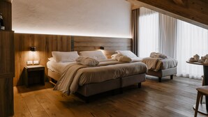 A bedroom with two beds, wooden flooring, a nightstand with a lamp, and a window with curtains. - Armon Greenblu Hotel & Wellness (Dimaro Folgarida)