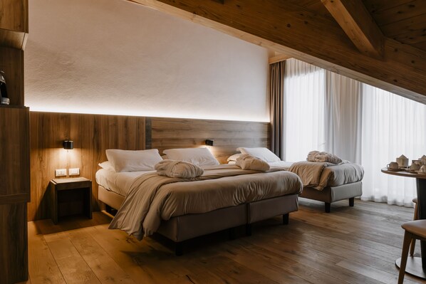 A bedroom with two beds, wooden flooring, a nightstand with a lamp, and a window with curtains. - Armon Greenblu Hotel & Wellness (Dimaro Folgarida)