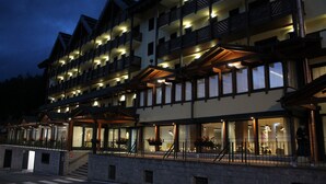 A multi-story hotel with balconies, large windows, and a stone facade. - Armon Greenblu Hotel & Wellness (Dimaro Folgarida)