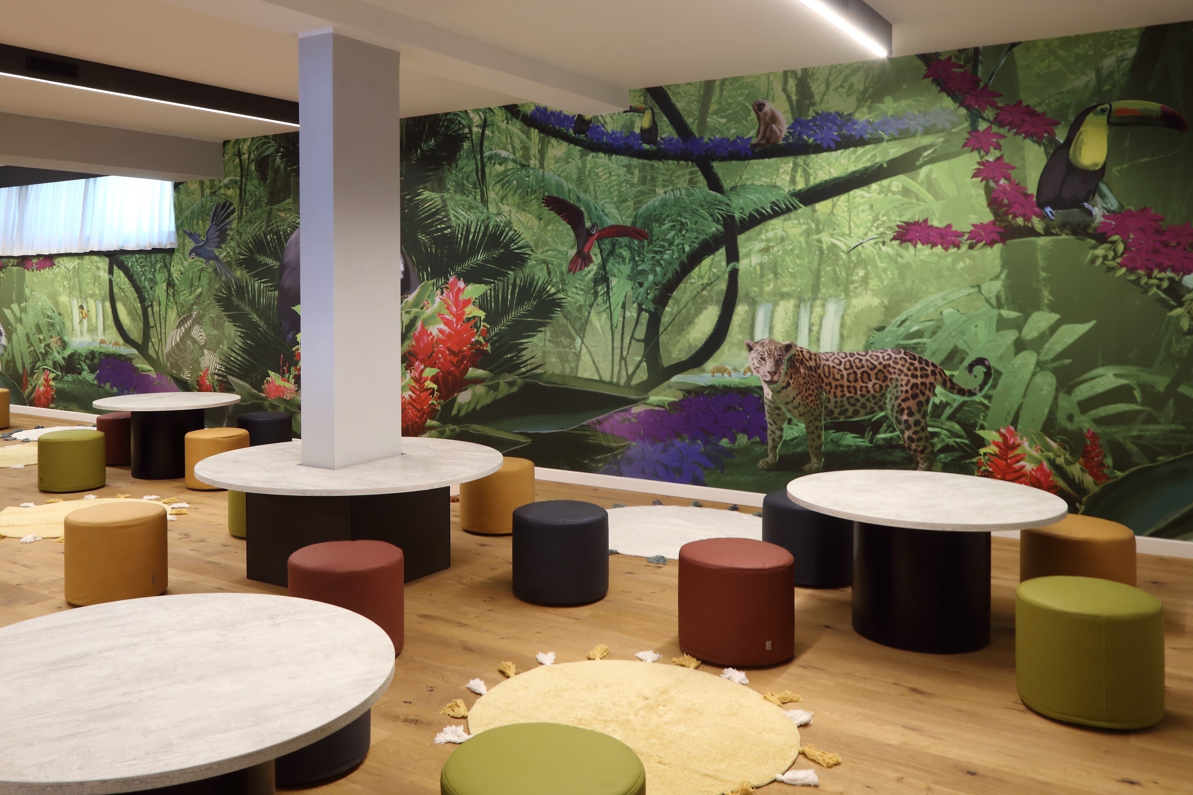 A room with round tables and stools, a mural of a jungle scene, and a large white pillar.