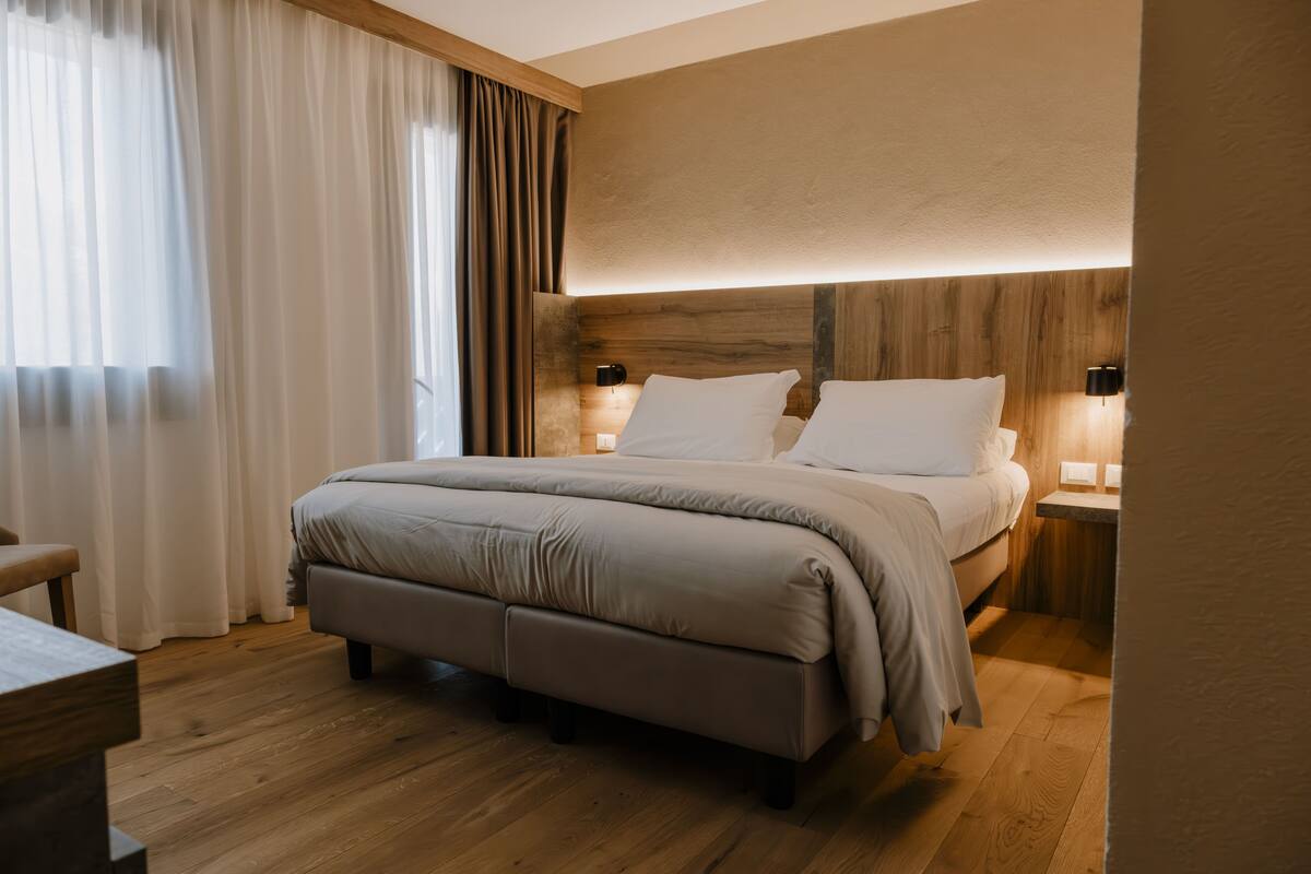 A modern bedroom with a large bed, wooden headboard, bedside lamps, and a wooden floor.