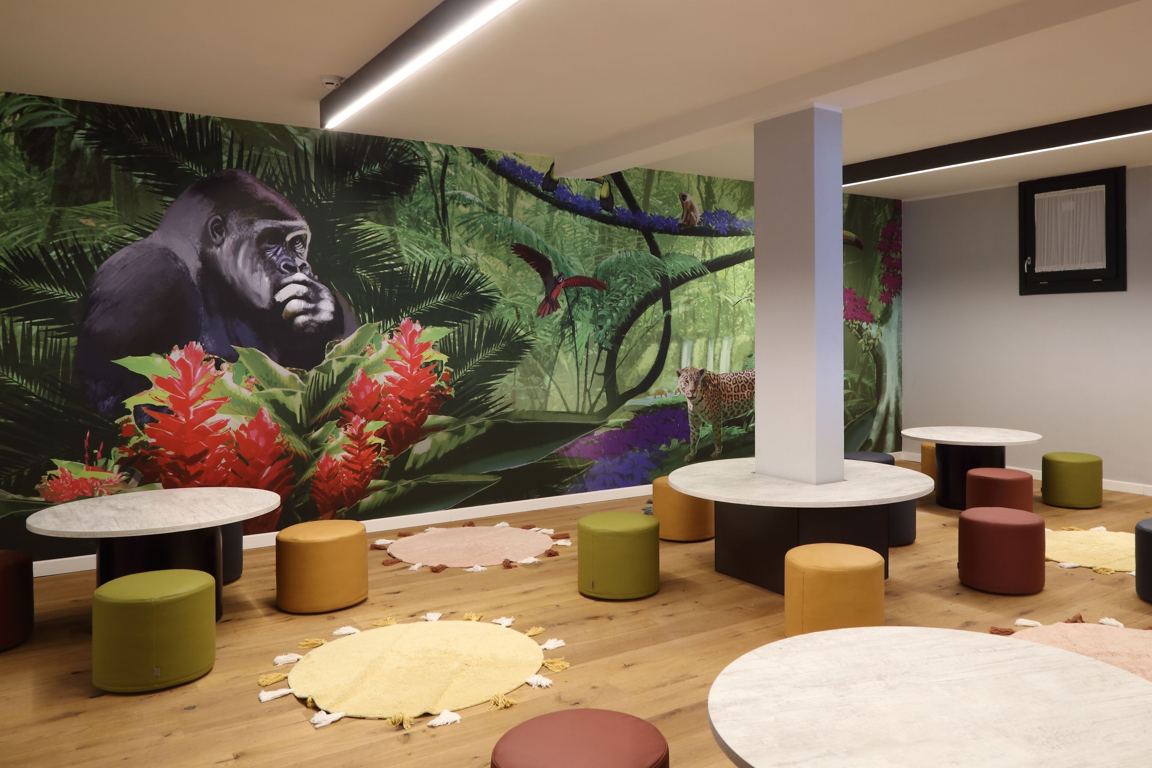 Una habitación con un gran mural de un gorila y una escena de selva, mesas redondas y taburetes.