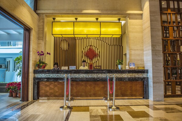 A reception desk with a receptionist, a decorative wall, and a check-in counter.
