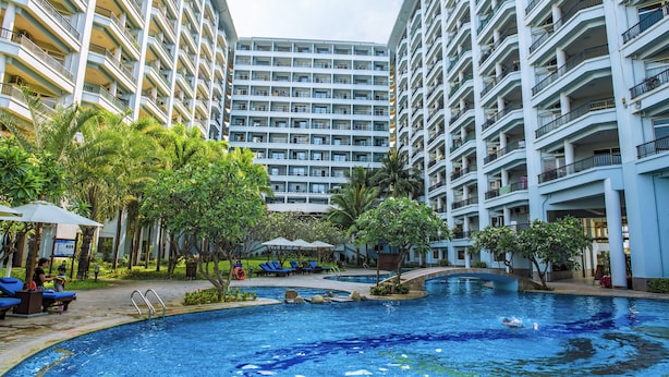 Un hotel con varios balcones, piscina y abundante vegetación.