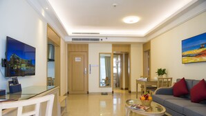 Una habitación de hotel moderna con comedor, sala de estar con sofá y mesa de centro, y un televisor montado en la pared.