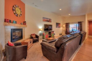 A living room with a fireplace, leather sofa, television, and artwork on the walls.