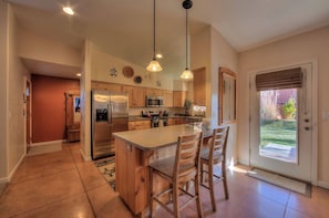 A kitchen with a central island, wooden cabinets, stainless steel appliances, pendant lighting, and a view to the outside.