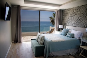 Enjoy ocean views from the large window, featuring a comfortable bed, a green bench, and a flat-screen TV.