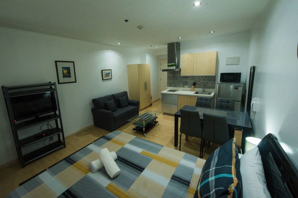 A compact living space with a sofa, TV, dining table, and kitchenette.