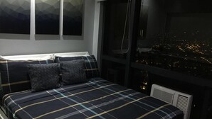 A bedroom with a bed, a window with a city view, and a radiator. - Seven Doors in Gramercy Makati (Makati)