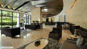 A spacious lobby with a modern design, featuring a reception desk, seating areas, and large windows offering a view of the outdoors. - Seven Doors in Gramercy Makati (Makati)