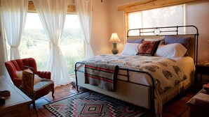 A bedroom with a bed, a chair, a lamp, and a view of the outdoors.