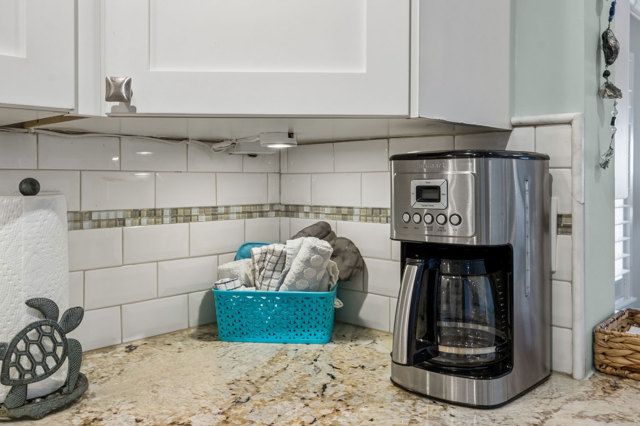 A kitchen with white cabinets, a coffee maker, a blue laundry basket, and a decorative turtle.
