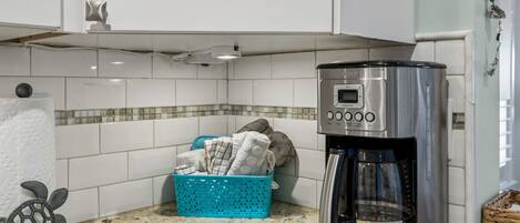 A kitchen with white cabinets, a coffee maker, a blue laundry basket, and a decorative turtle.