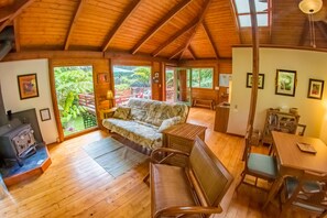 A spacious room with a high wooden ceiling, a sofa, a dining table, and a view of lush greenery outside. - 8 minutes to Nat'l Park! Enjoy the sound of rain & birds in a peaceful retreat. (Volcano)