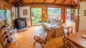 A cozy cabin interior with a wooden floor, a sofa, a TV, and a fireplace. - 8 minutes to Nat'l Park! Enjoy the sound of rain & birds in a peaceful retreat. (Volcano)