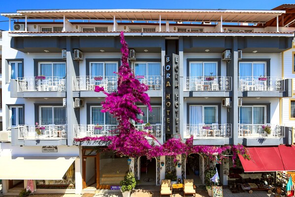 A hotel with multiple balconies, a prominent entrance, and a large purple bougainvillea plant in front. - Bora Hotel (Datça)
