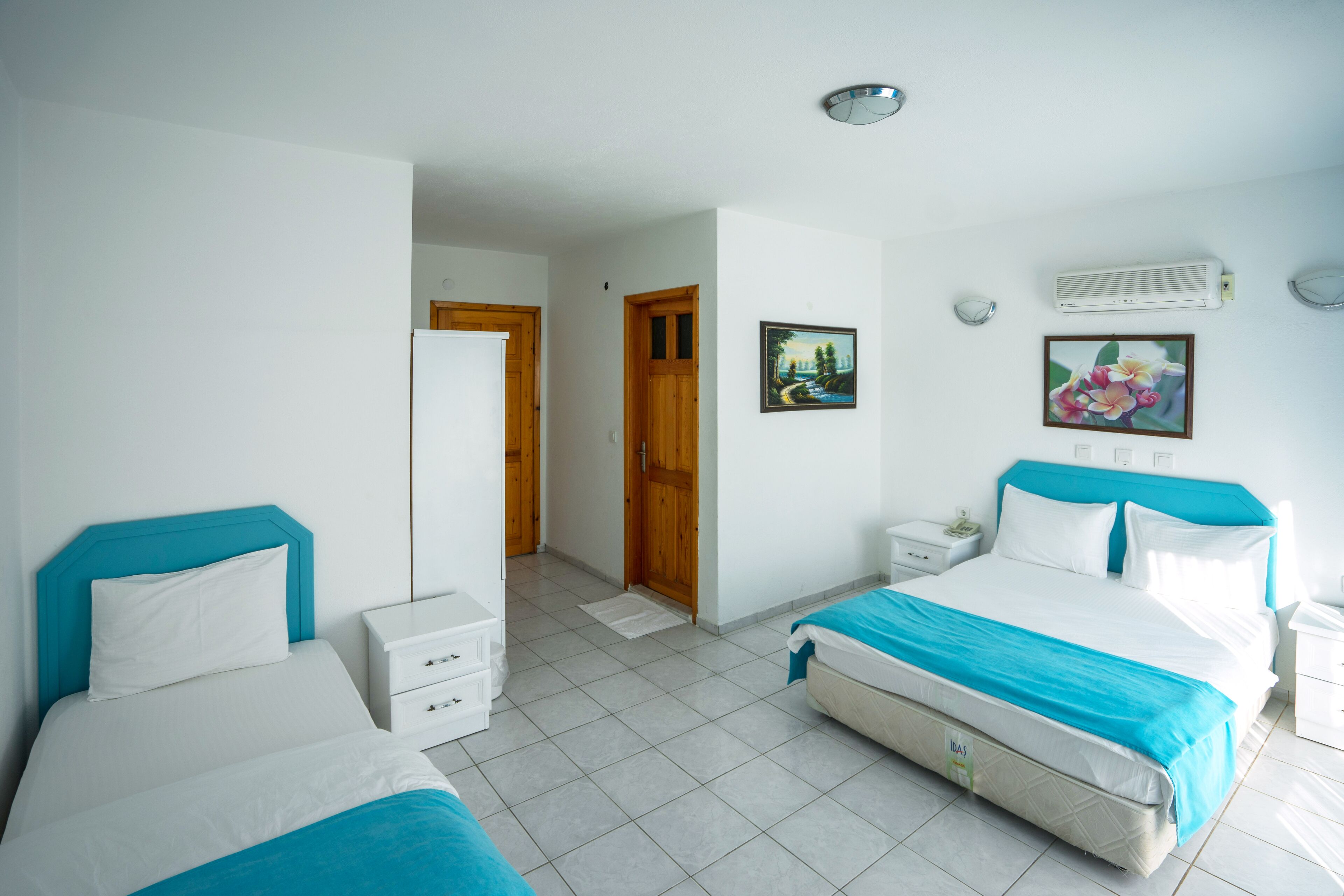 A hotel room with two beds, a white tiled floor, wooden doors, and a white air conditioning unit.