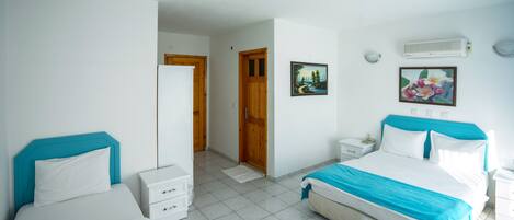 A hotel room with two beds, a white tiled floor, wooden doors, and a white air conditioning unit.