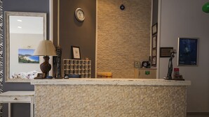 Un comptoir d’accueil avec un mur en pierre à texture, une horloge, des tableaux encadrés et une lampe.