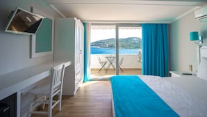 Une chambre d’hôtel comprenant un lit, un bureau avec une chaise, une télévision et une vue sur la mer, accessible par une porte-fenêtre coulissante.