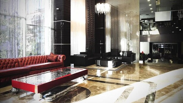 A spacious lobby with a red sofa, black armchairs, a marble coffee table, and a chandelier. - Demora Hotel (Ankara)