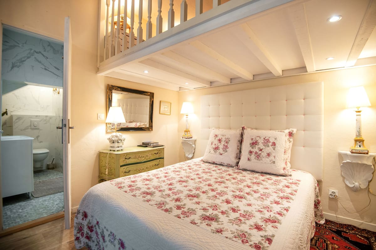 A bedroom with a large bed, two bedside lamps, a mirror, and a wooden ceiling.