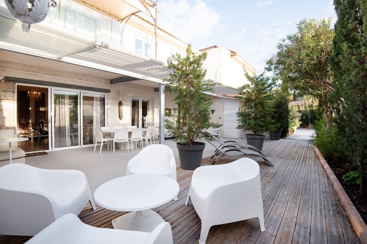 An outdoor patio with white plastic furniture, potted plants, and a wooden deck.