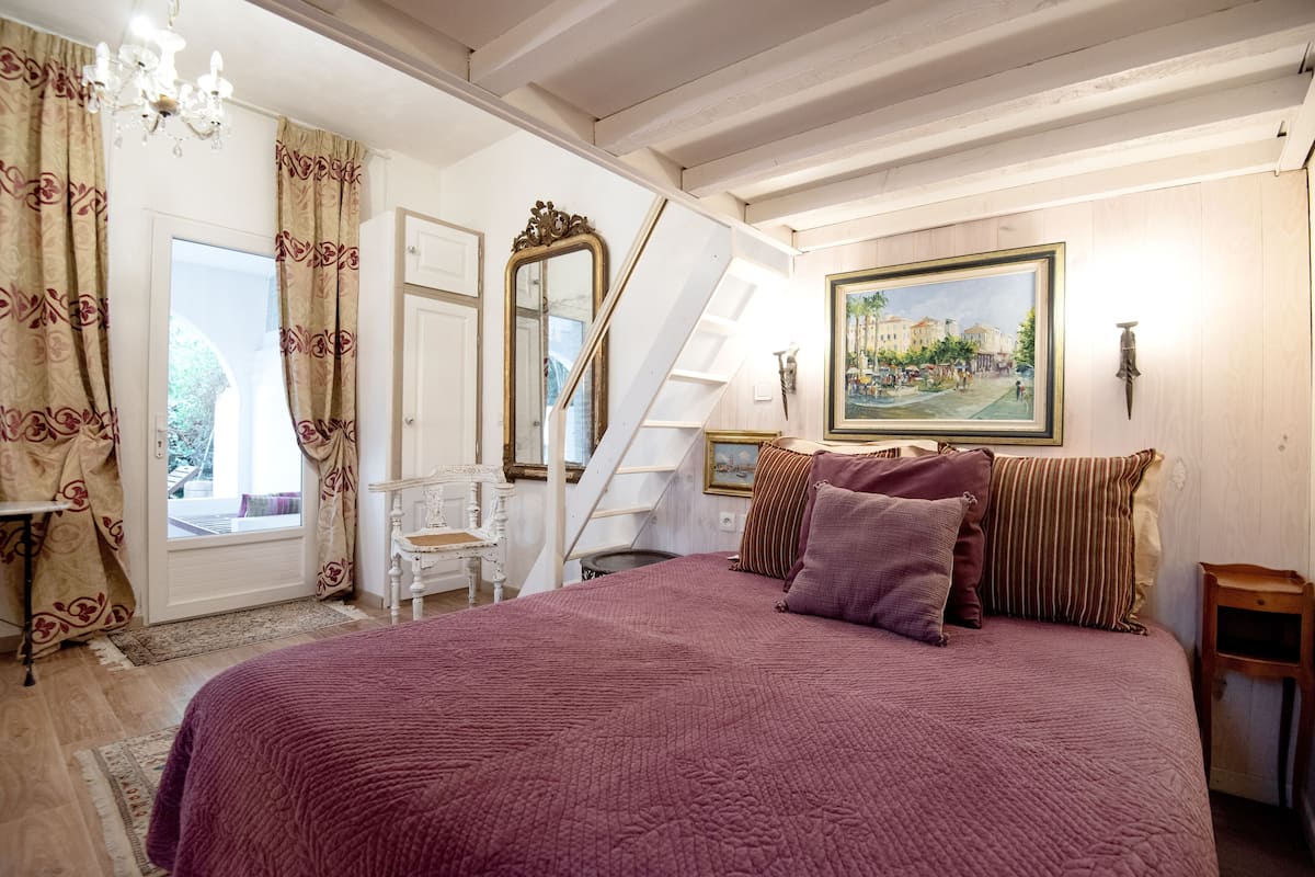 A bedroom with a large bed, a staircase, a painting, and a chandelier.