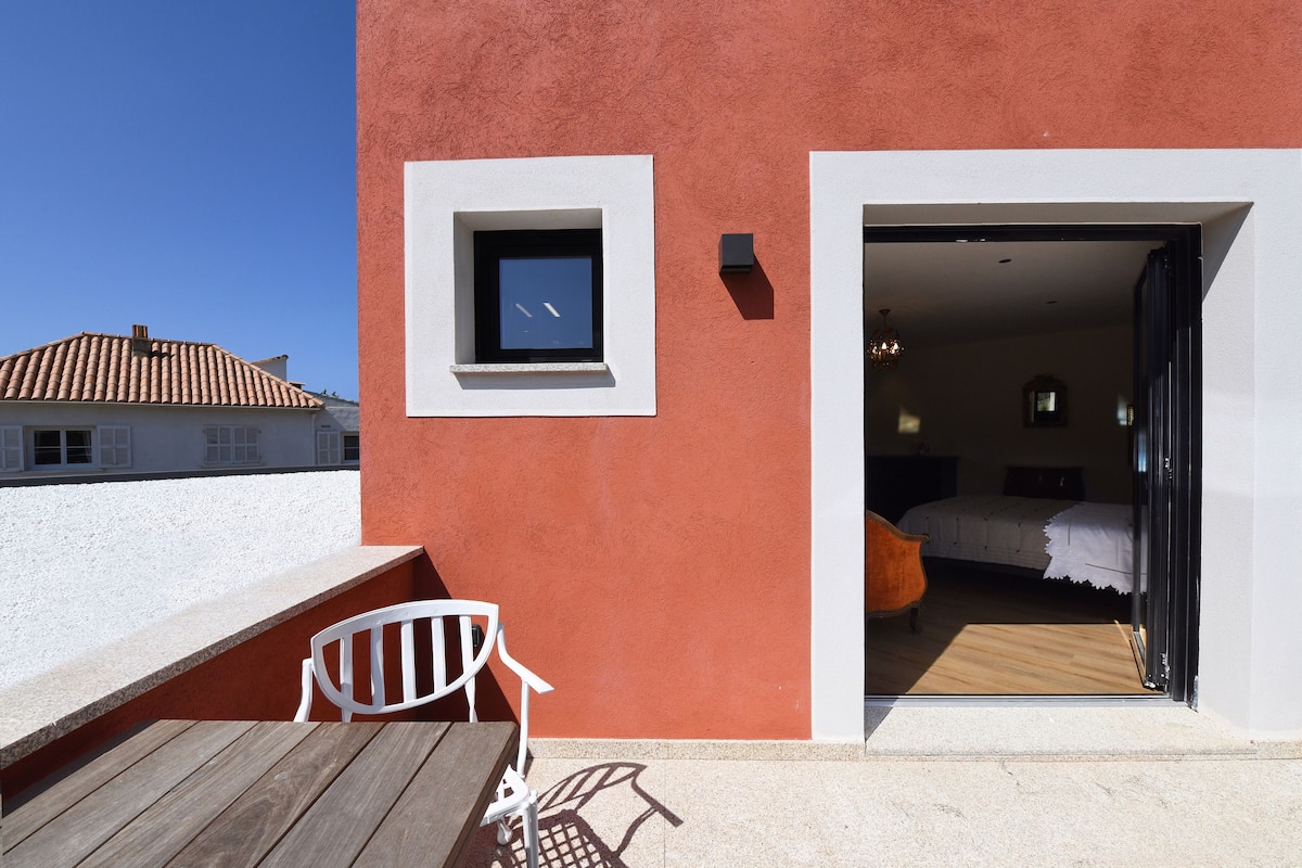 A room with a bed, a small window, and a door leading to an outdoor area with a table and chairs.