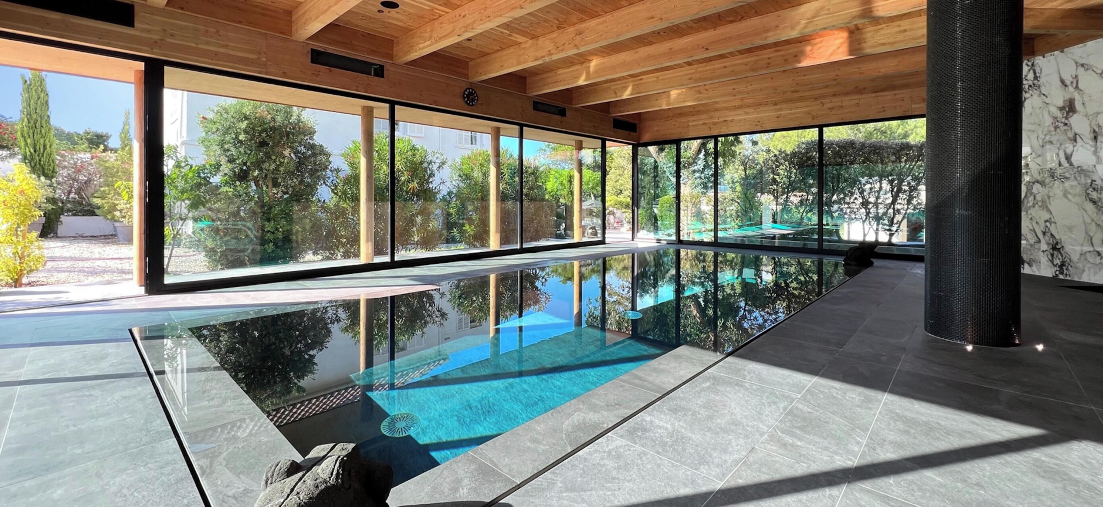 A modern indoor swimming pool with large windows and a wooden ceiling.