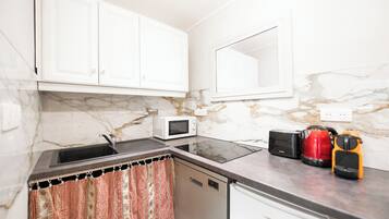 Una cocina con armarios blancos, microondas, tostadora y hervidor sobre el mostrador.
