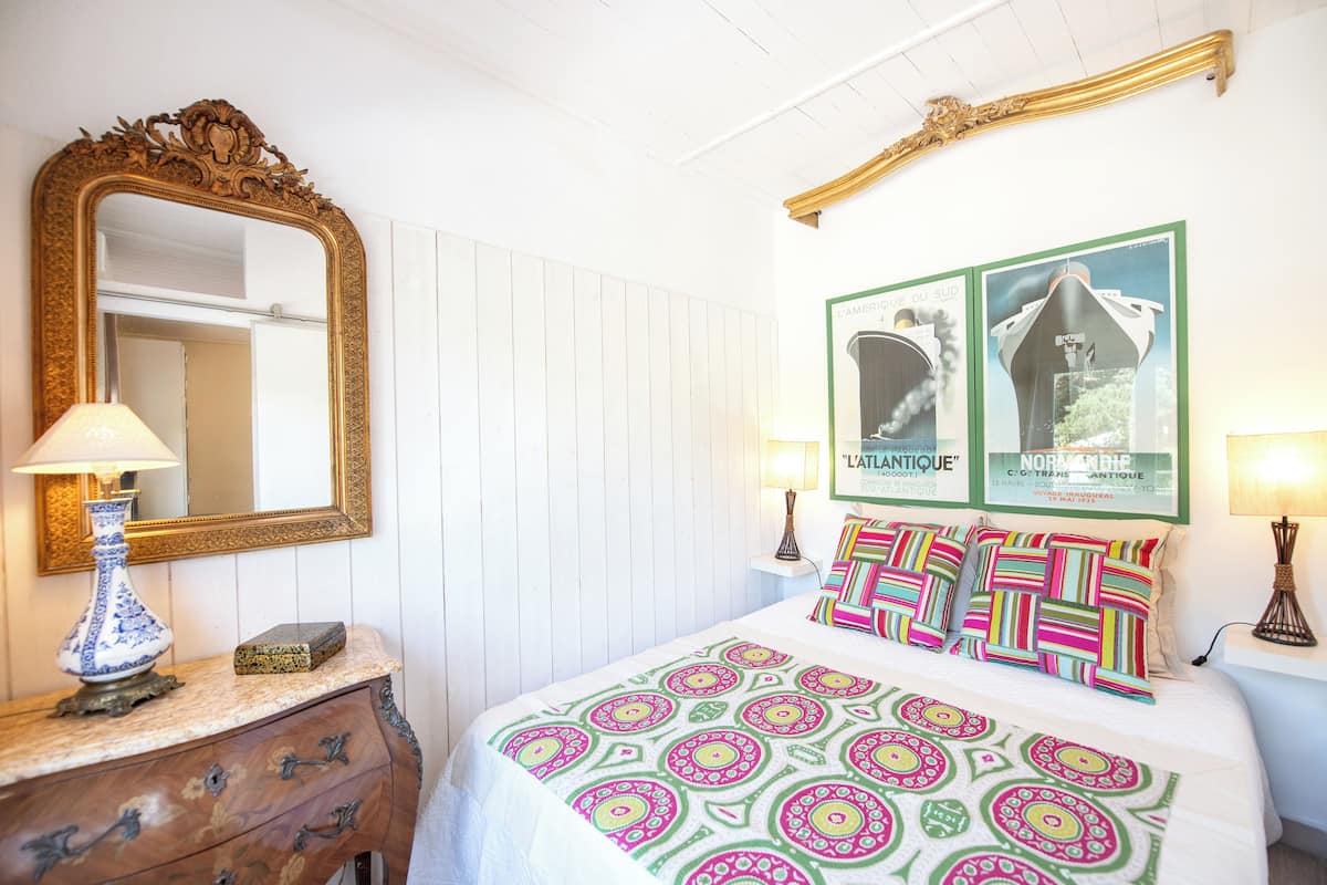 A bedroom with a bed, a dresser, a mirror, and two framed pictures on the wall.